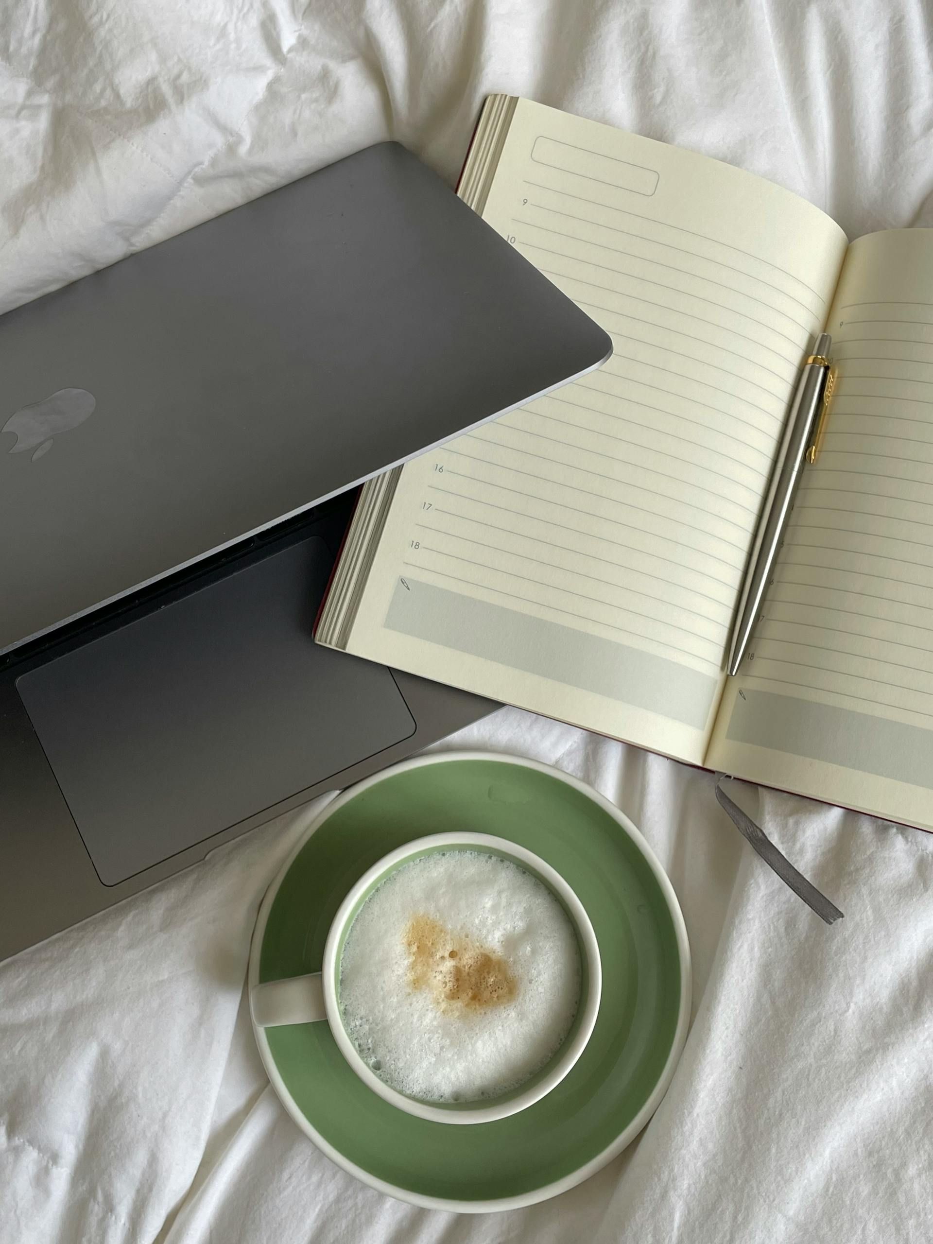 Laptop, notebook, and cup of coffee on a white surface