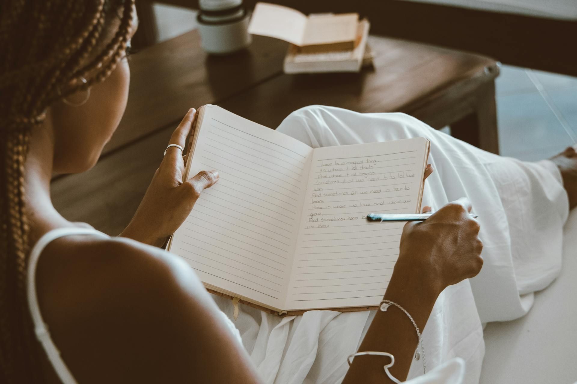Person sitting on a couch writing in a notebook with a pen.