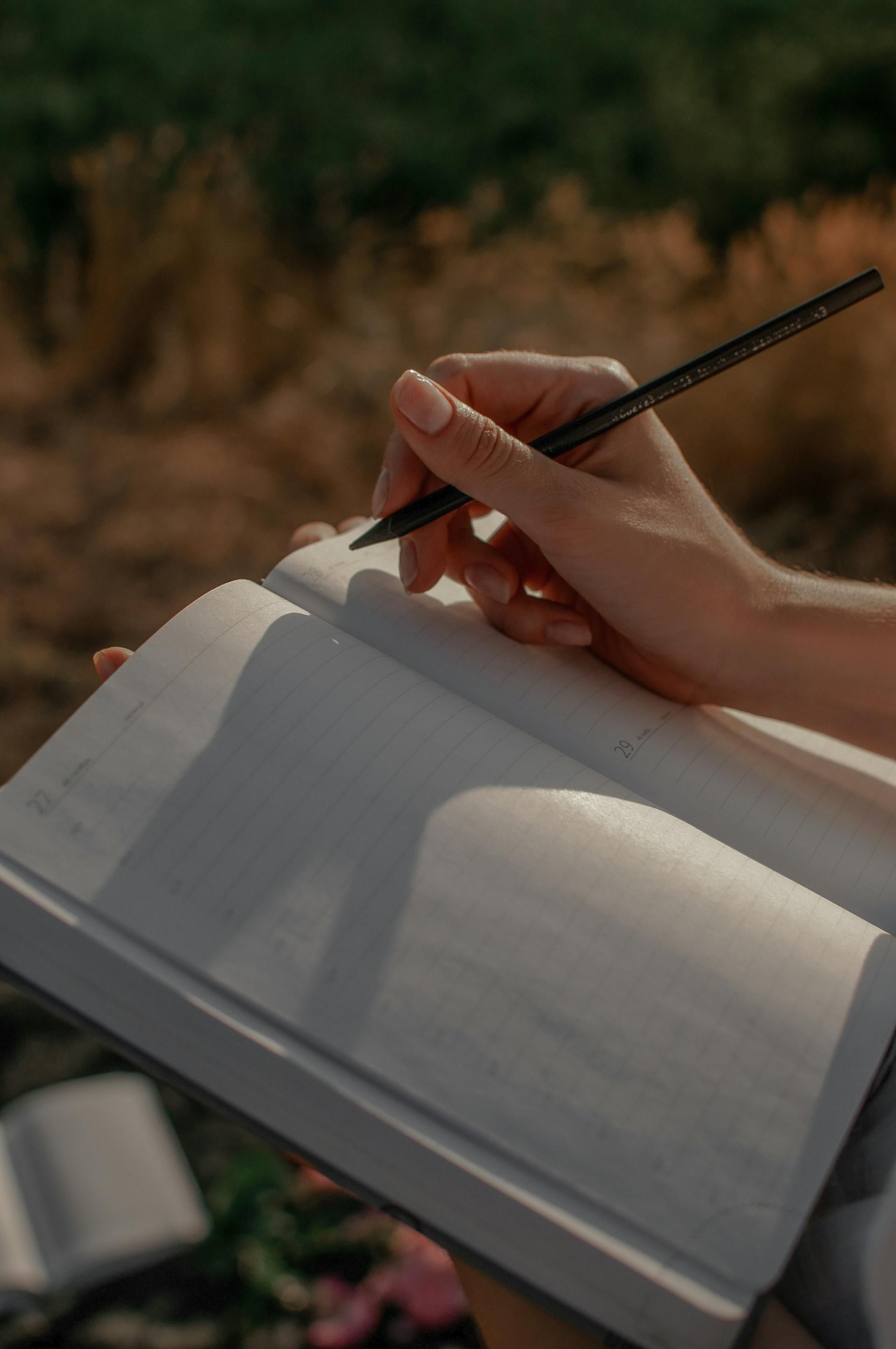 Hand holding a pen over an open notebook with a blurred natural background