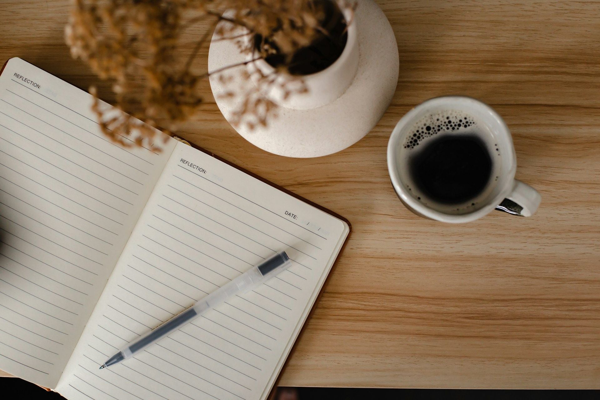 Open notebook with pen, cup of coffee, and small plant on a wooden table