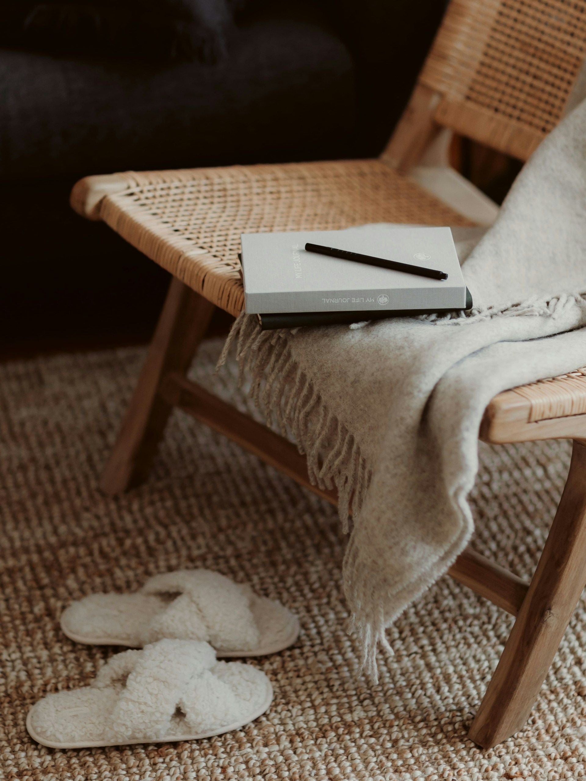 Wicker chair with a blanket, notebook, and pen on a textured rug.